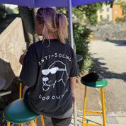 Person wearing an 'Anti-Social Dog Owner' t-shirt sitting under a purple umbrella.